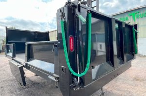Black dump body with one side folded down. Rear gate with latch shown.